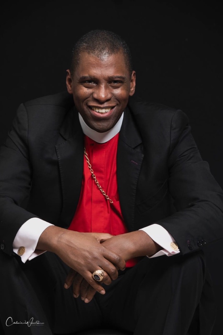 Bishop H. Curtis Douglas, smiling, in a black suit and red clerical shirt with a pectoral cross.