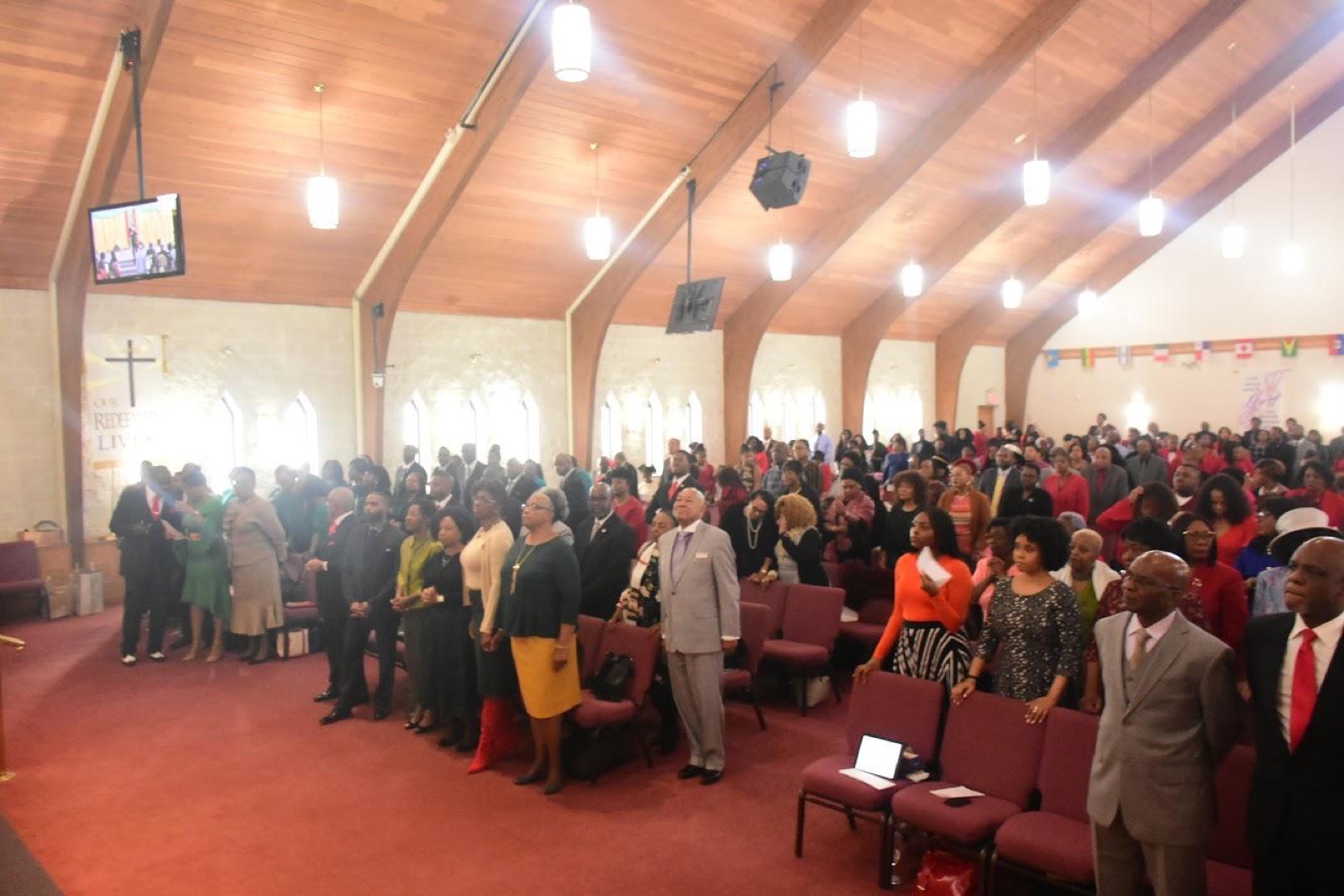 A packed sanctuary, the congregation standing in prayer during Sunday worship.