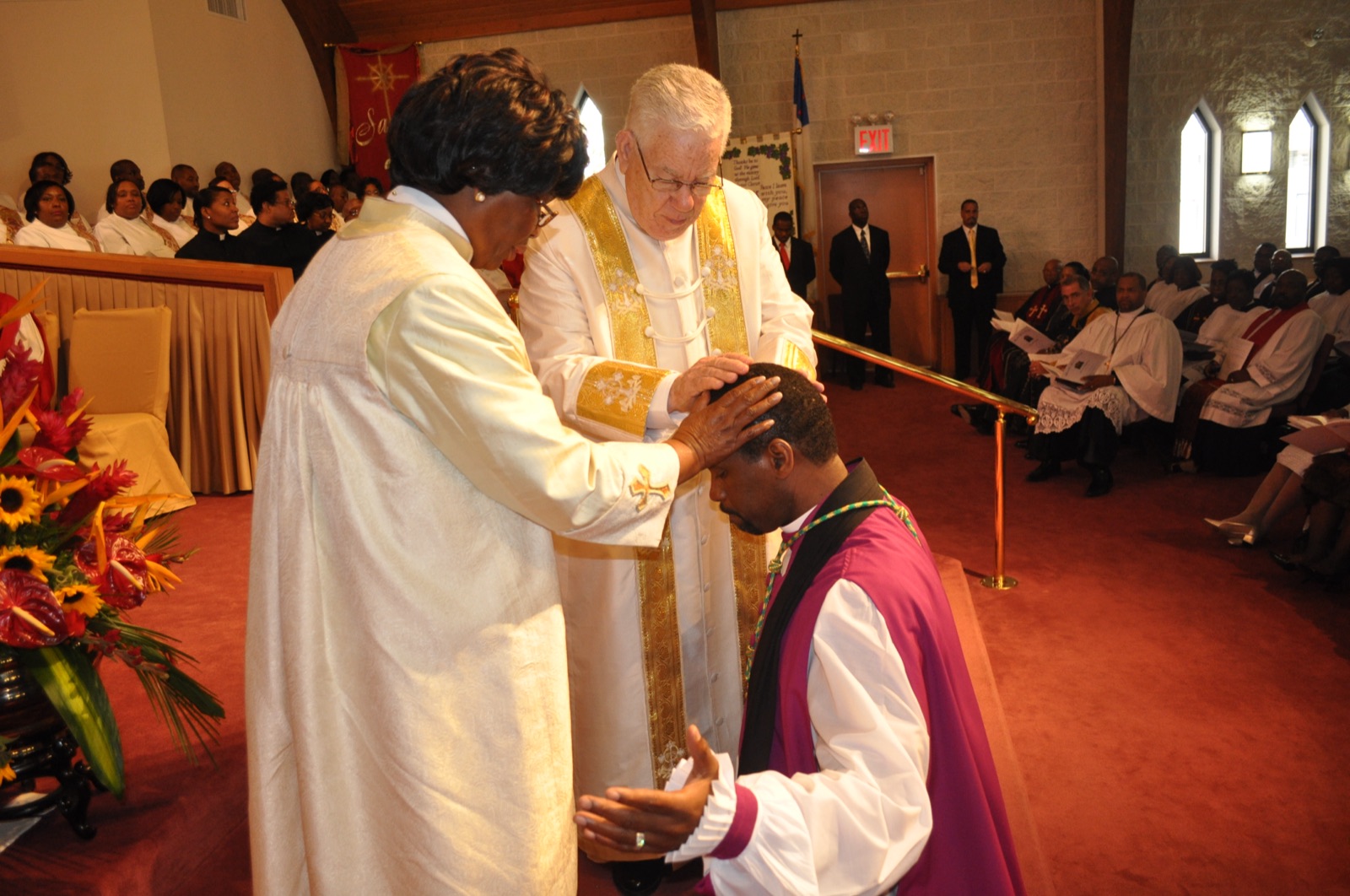 A minister kneels as clergy lay hands on him in prayer during an ordination service.
