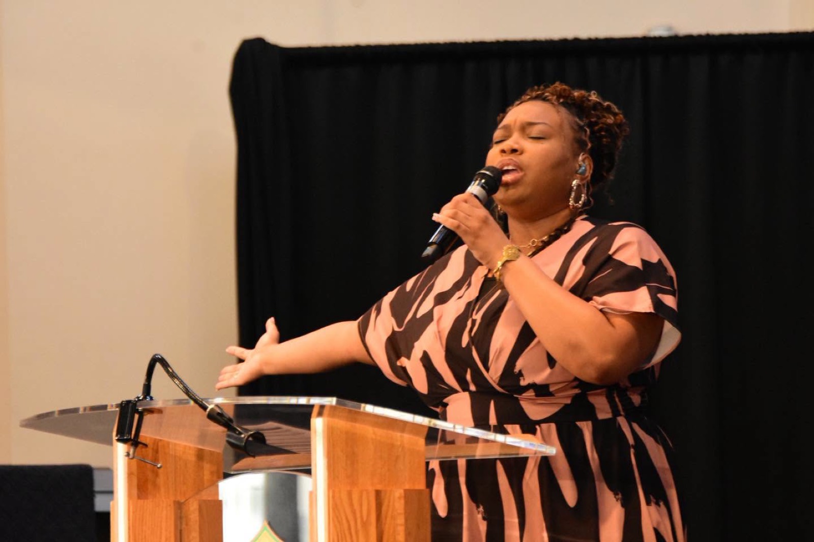 A worship leader sings at the clear pulpit, arm outstretched.