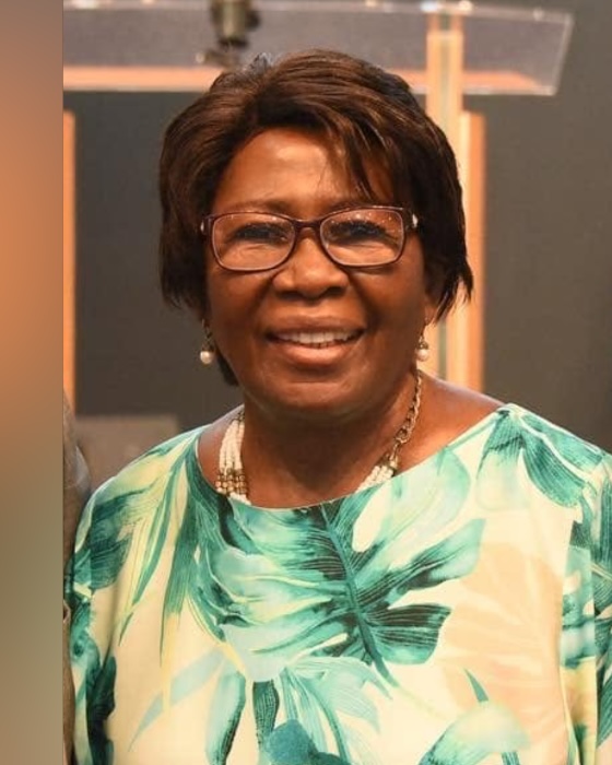 Portrait of Rev. Lenore Kidd, smiling, in glasses and a green patterned top.